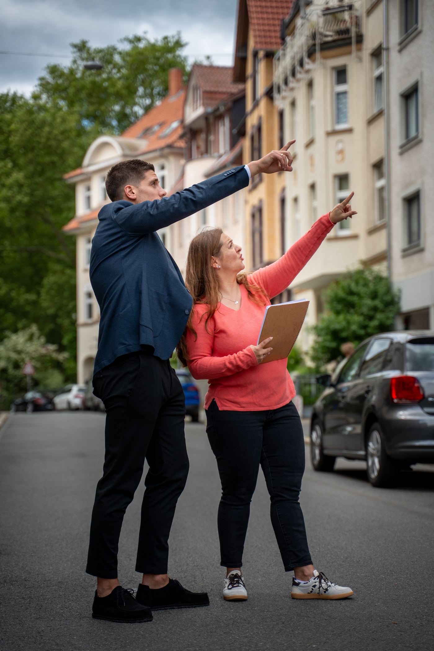 Zwei Hausverwaltungsexperten zeigen gemeinsam auf ein Gebäude in einer Altbaustraße – Objektbegehung im Rahmen einer professionellen Verwaltung 