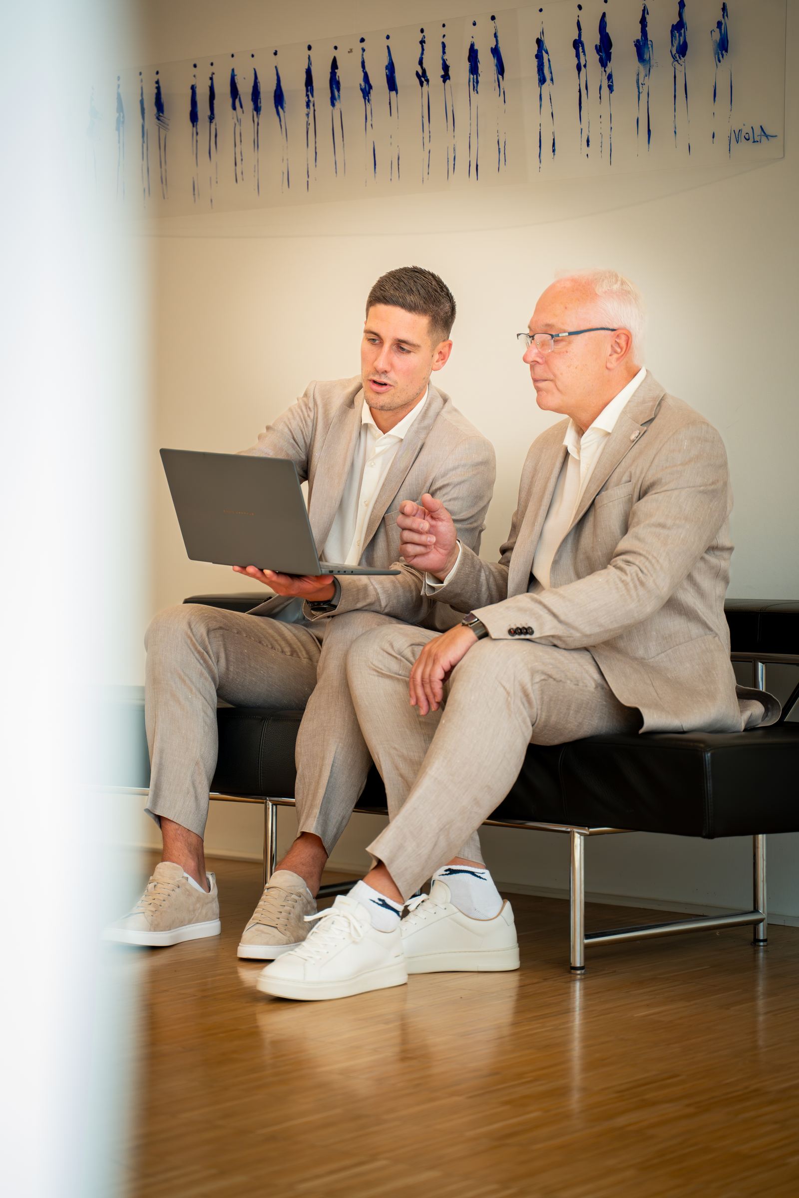 Zwei Mitarbeiter sitzen gemeinsam auf einer Couch und besprechen Details am Laptop – enge Zusammenarbeit bei Volksbank Immobilien GmbH Kassel Göttingen