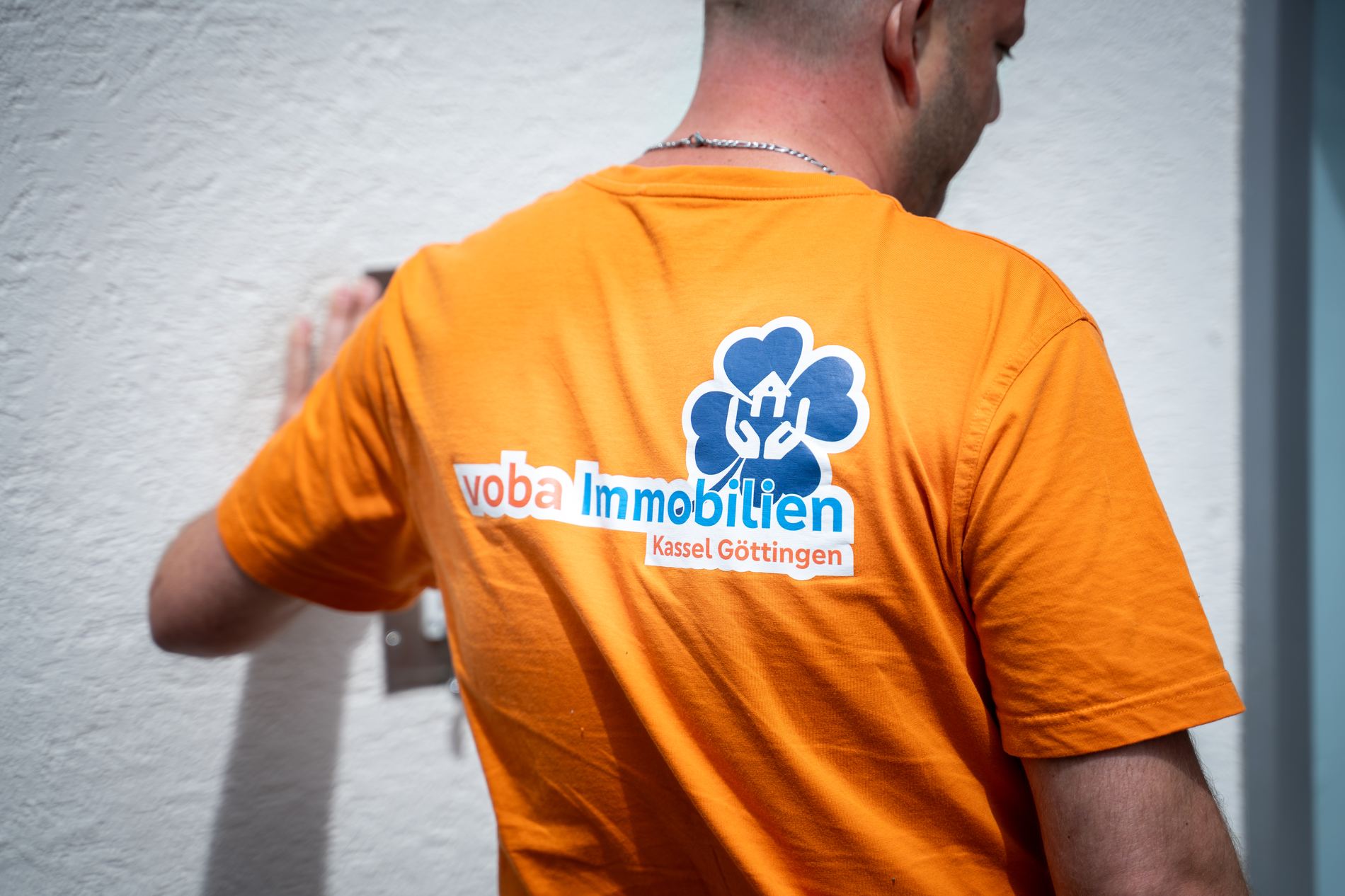 Mitarbeiter im orangenen T-Shirt mit Firmenlogo und Markenname "voba Immobilien Kassel Göttingen"