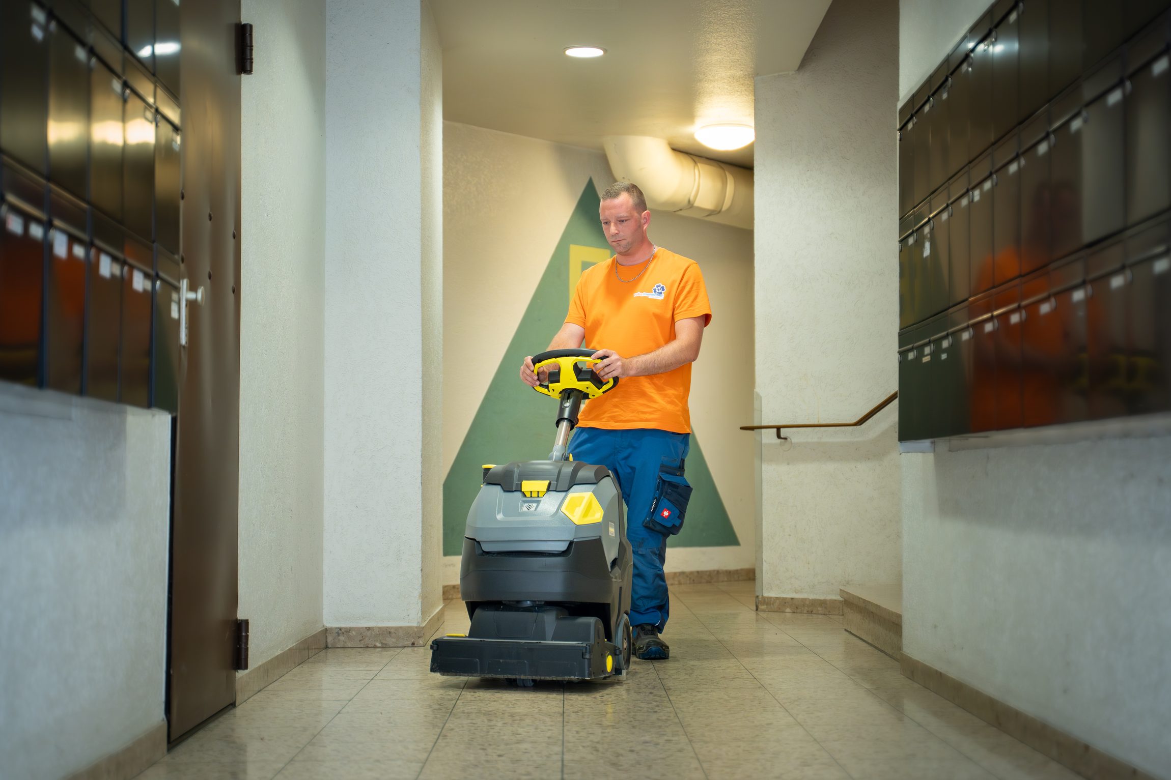 Mitarbeiter reinigt mit professioneller Scheuersaugmaschine den Flur eines Mehrfamilienhauses – Gebäudeservice von Volksbank Immobilien Kassel Göttingen