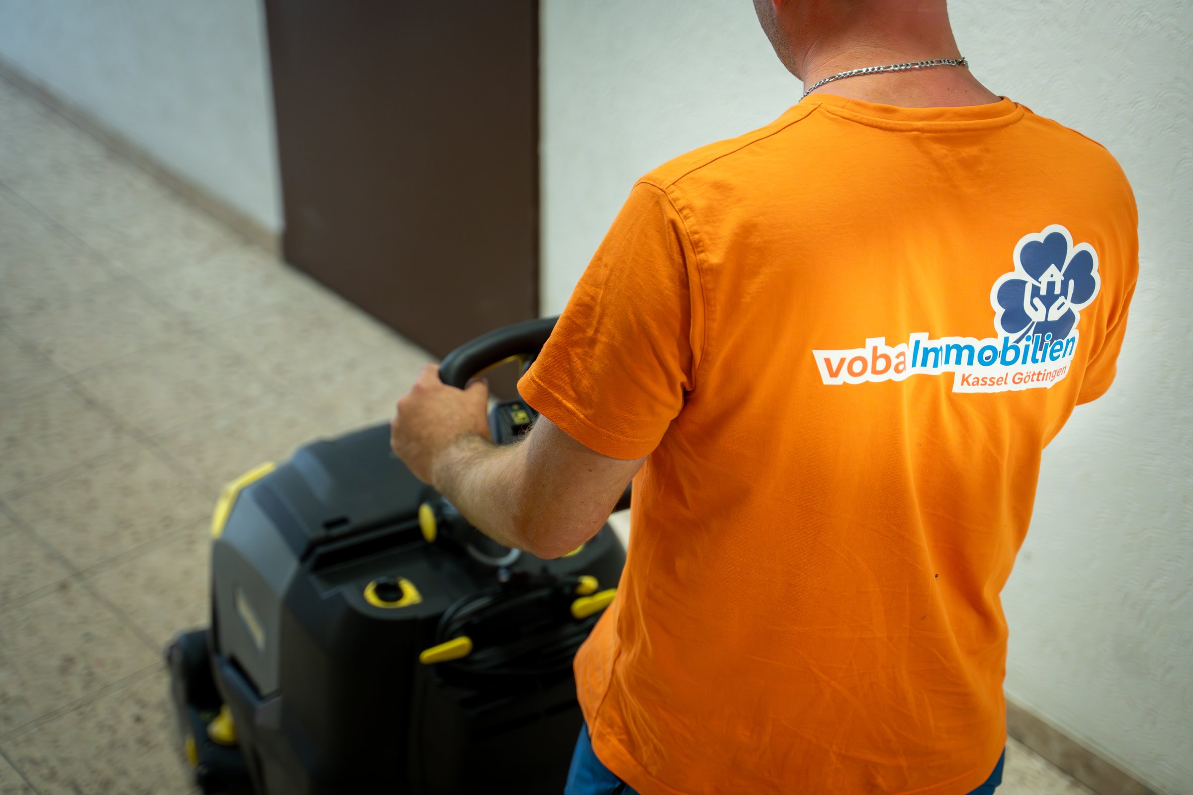 Mitarbeiter im Firmenshirt schiebt eine professionelle Reinigungsmaschine durch einen Hausflur – Facility Management von Volksbank Immobilien Kassel Göttingen