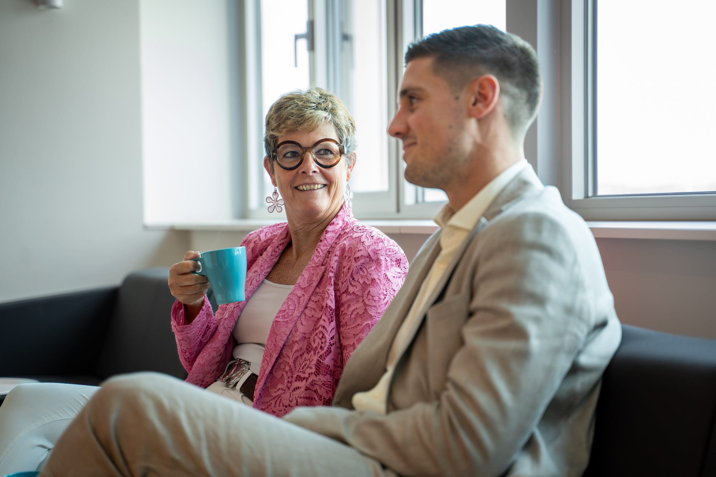 Mitarbeiterin mit Kaffeetasse im Gespräch mit einem Kollegen in einer Sitzecke 