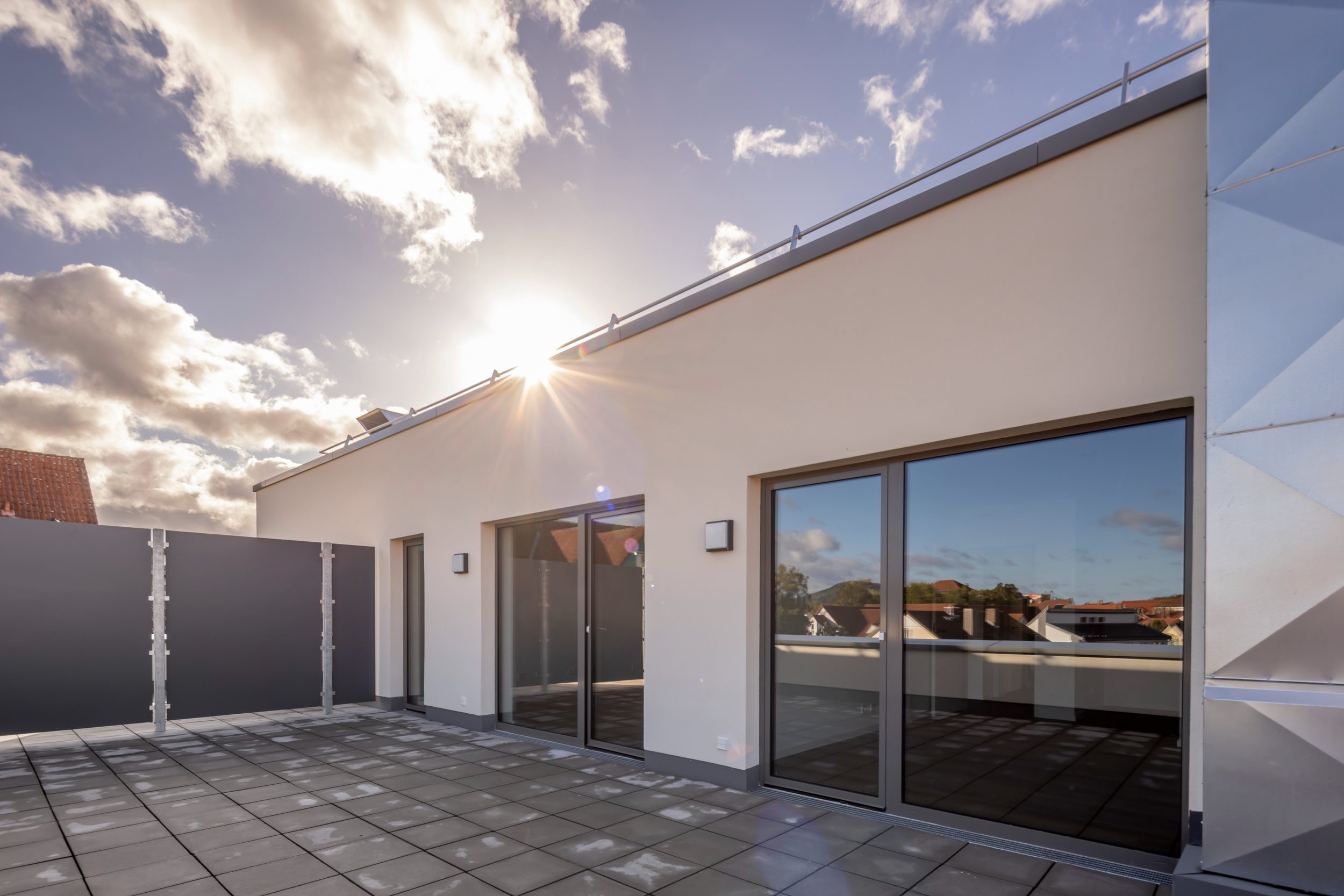 Moderne Dachterrasse einer Eigentumswohnung mit Sichtschutz und großzügigen Glastüren als Teil eines Immobilien Portfolios
